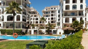 A pool area with lounge chairs and palm trees, surrounded by multi-story white buildings with balconies. - Marina Duquesa 2110 Lovely Place (Manilva)