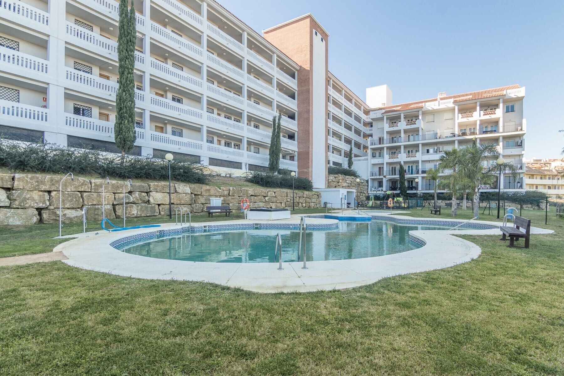 A hotel with multiple balconies, a swimming pool, and a stone wall.