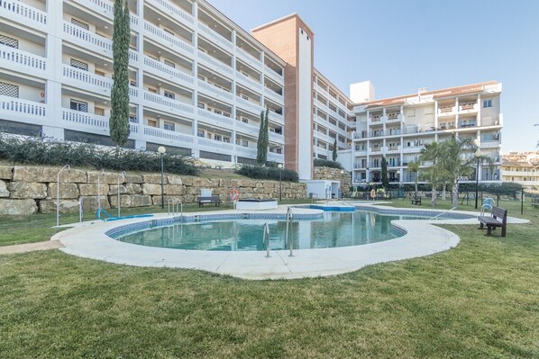 A hotel with multiple balconies, a swimming pool, and a stone wall.