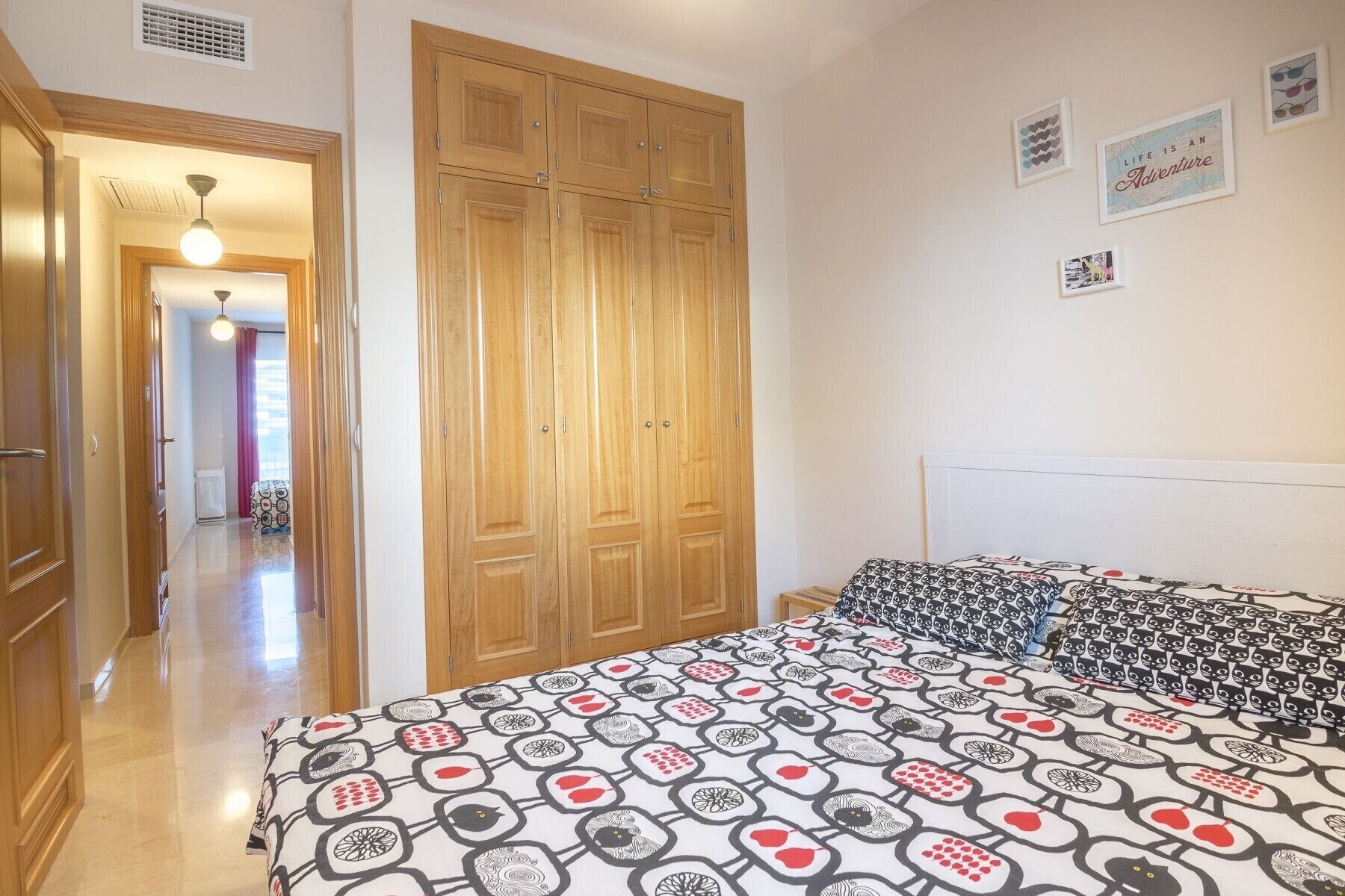 A bedroom with a bed, wooden wardrobe, and a hallway leading to another room.