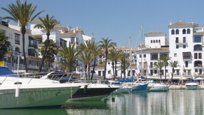 A marina with several boats docked, surrounded by white buildings with balconies and palm trees.