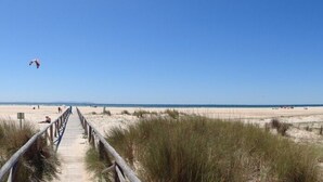 A beach with a wooden boardwalk leading to the shore, sandy dunes, and a clear blue sky.