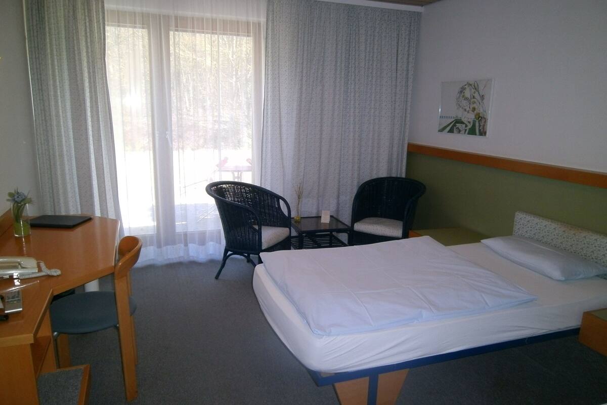 A hotel room with a bed, a desk with a telephone, two chairs, and a small table.