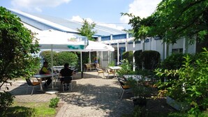 An outdoor patio area with tables and chairs, a covered seating area, and a building with a blue roof in the background.