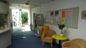 A reception area with wicker chairs, a small table with a plant, and a bulletin board with various notices.