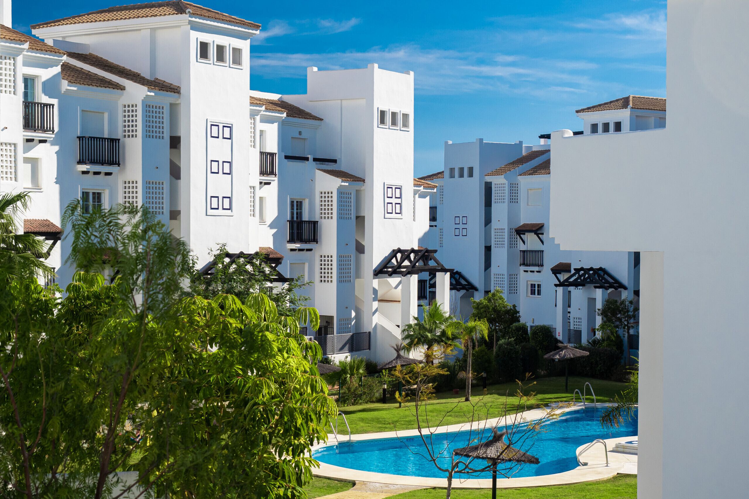 Een resort met witte gebouwen, een zwembad en weelderige groene beplanting.