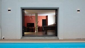 Une piscine donnant sur une pièce où l’on peut apercevoir un piano, une chaise et une plante.