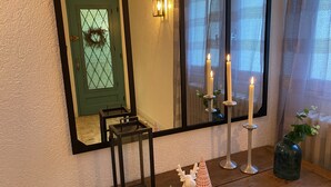 Un miroir reflétant une porte verte ornée d’une guirlande, un chandelier allumé et un petit vase blanc contenant une plante.