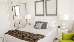A bedroom with a large bed, two bedside tables, a green chair, and two wall mirrors. - Metropole Apartments Old Town (Bucharest)