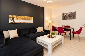 A modern living room with a black sectional sofa, a white coffee table, red chairs, and a dining table. There are two paintings on the walls. - Metropole Apartments Old Town (Bucharest)