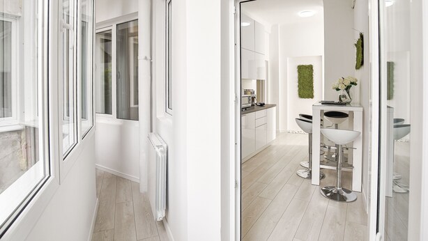 A modern, well-lit hallway with a radiator, leading to a kitchen area with white cabinets and a central island. - Metropole Apartments Old Town (Bucharest)