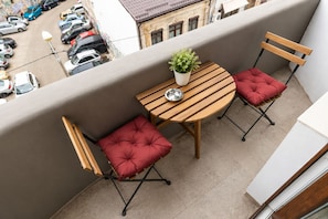 A balcony with a wooden table, two cushioned chairs, a potted plant, and a metal bowl. - Metropole Apartments Old Town (Bucharest)