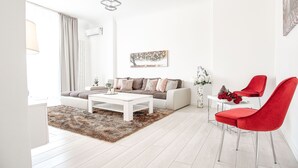 A modern living room with a white sofa, a white coffee table, and red chairs. There is a painting on the wall and a vase with flowers on a side table. - Metropole Apartments Old Town (Bucharest)
