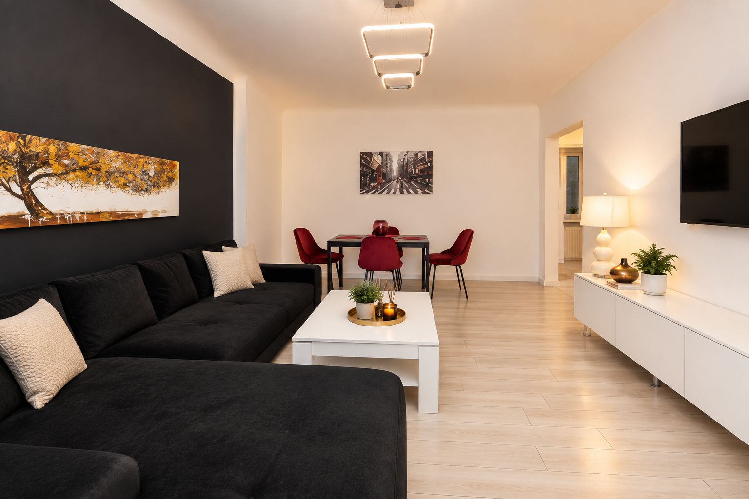 Ein modernes Wohnzimmer mit einem schwarzen Sofa, einem weißen Couchtisch und roten Stühlen. Es gibt eine Essecke mit einem roten Tisch und Stühlen, sowie ein an der Wand befestigtes Flachbildfernsehen.