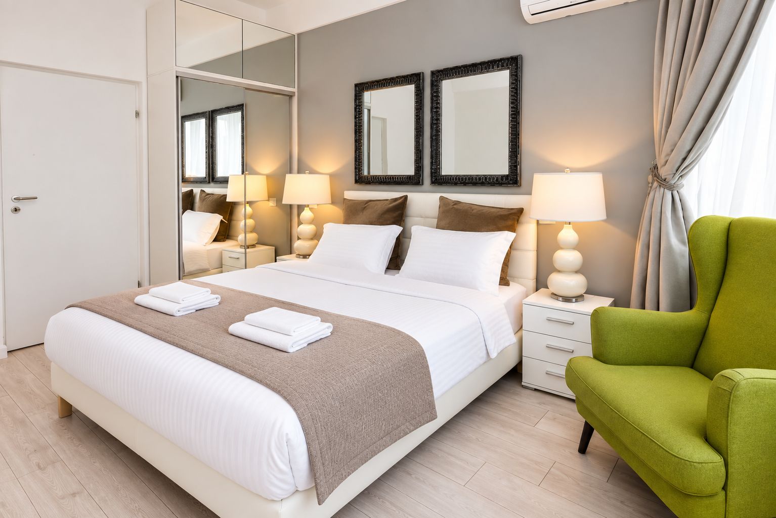 A hotel room with a large bed, two bedside tables, a green armchair, and a mirror on the wall.