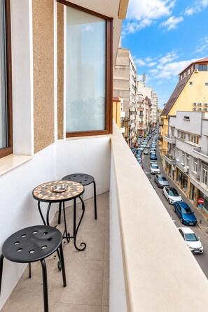 A balcony with a table and two chairs, overlooking a busy street with parked cars and buildings. - Metropole Apartments Old Town (Bucharest)