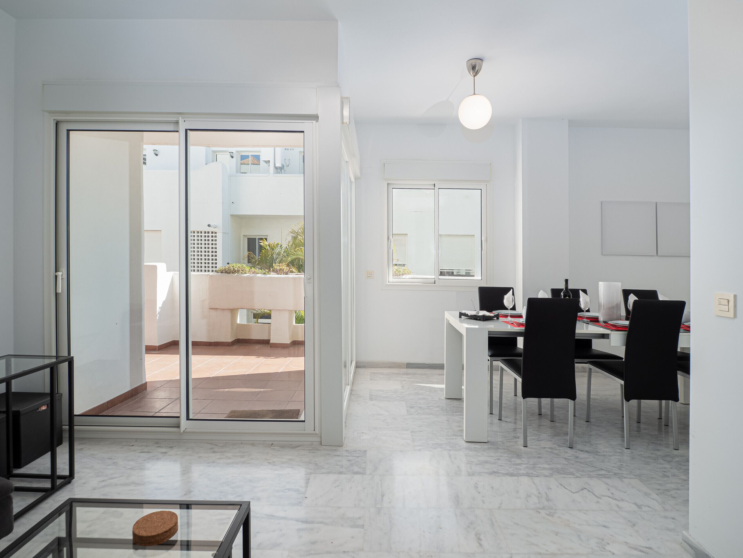 Een moderne, goed verlichte kamer met een eethoek, een schuifpui naar een balkon en uitzicht op de gevel.