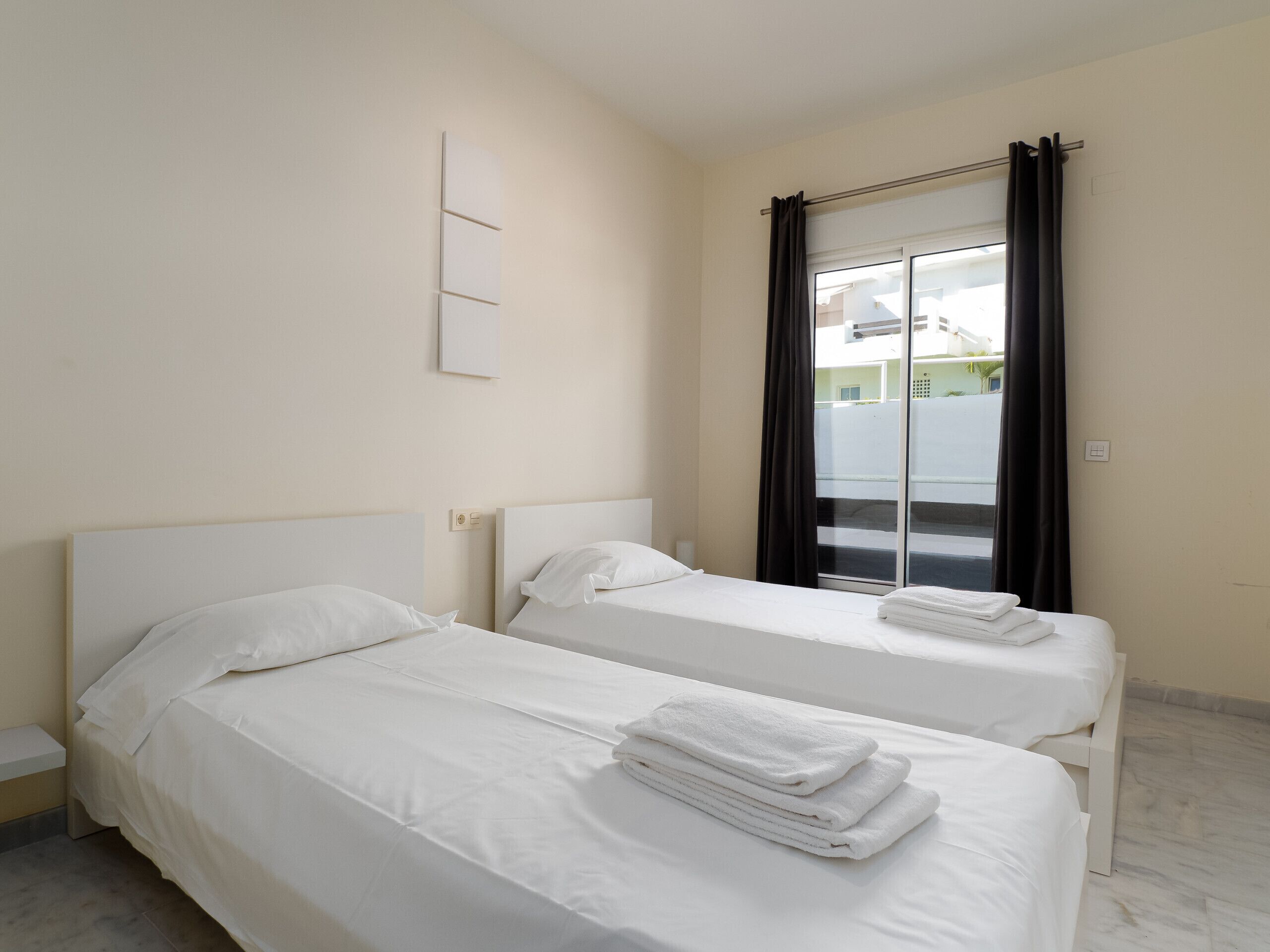 Una camera d'albergo con due letti singoli, un'ampia finestra con tende e vista sulla strada.