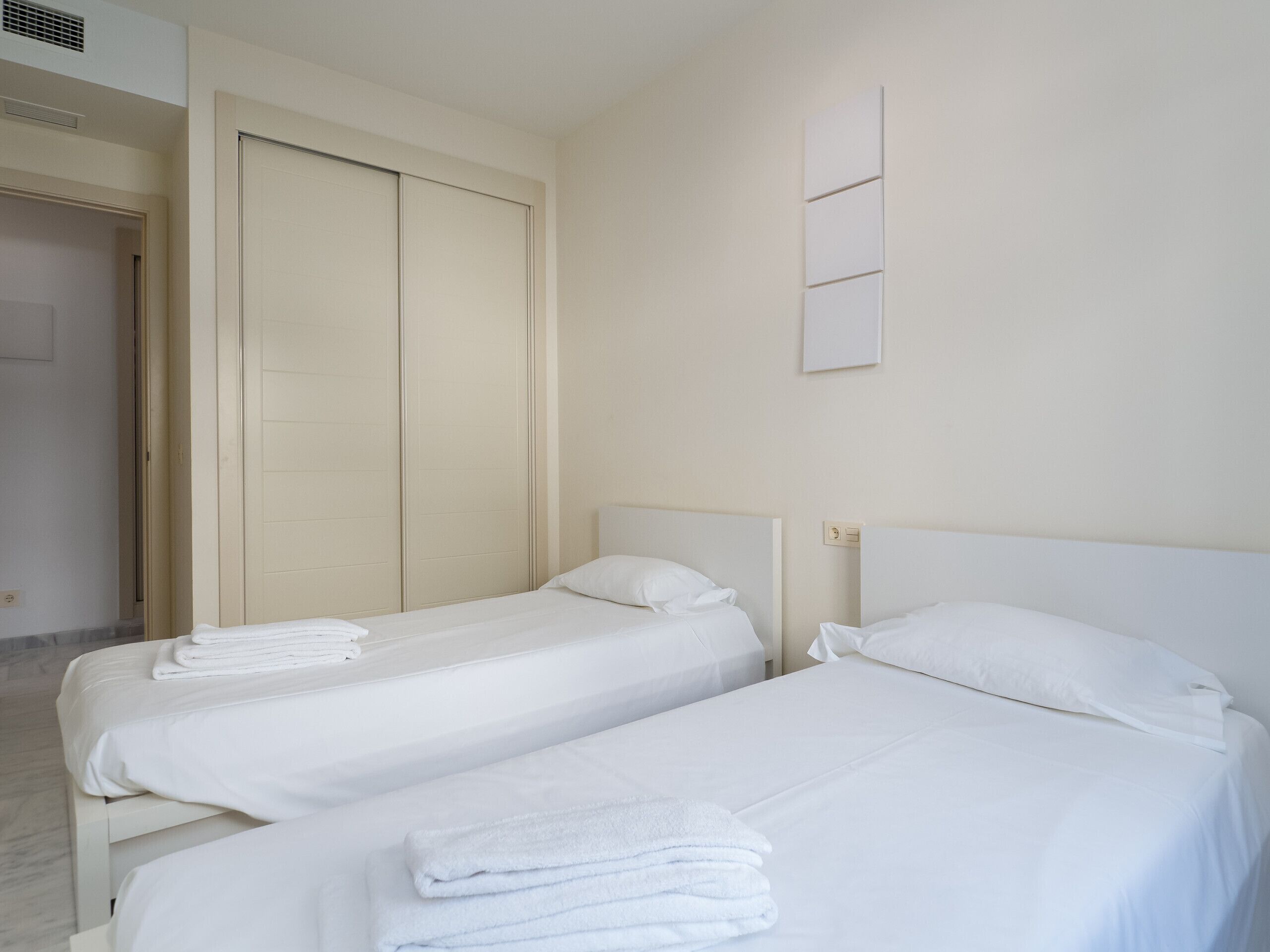 Habitación de hotel con dos camas individuales, un armario amplio y una lámpara fijada a la pared.