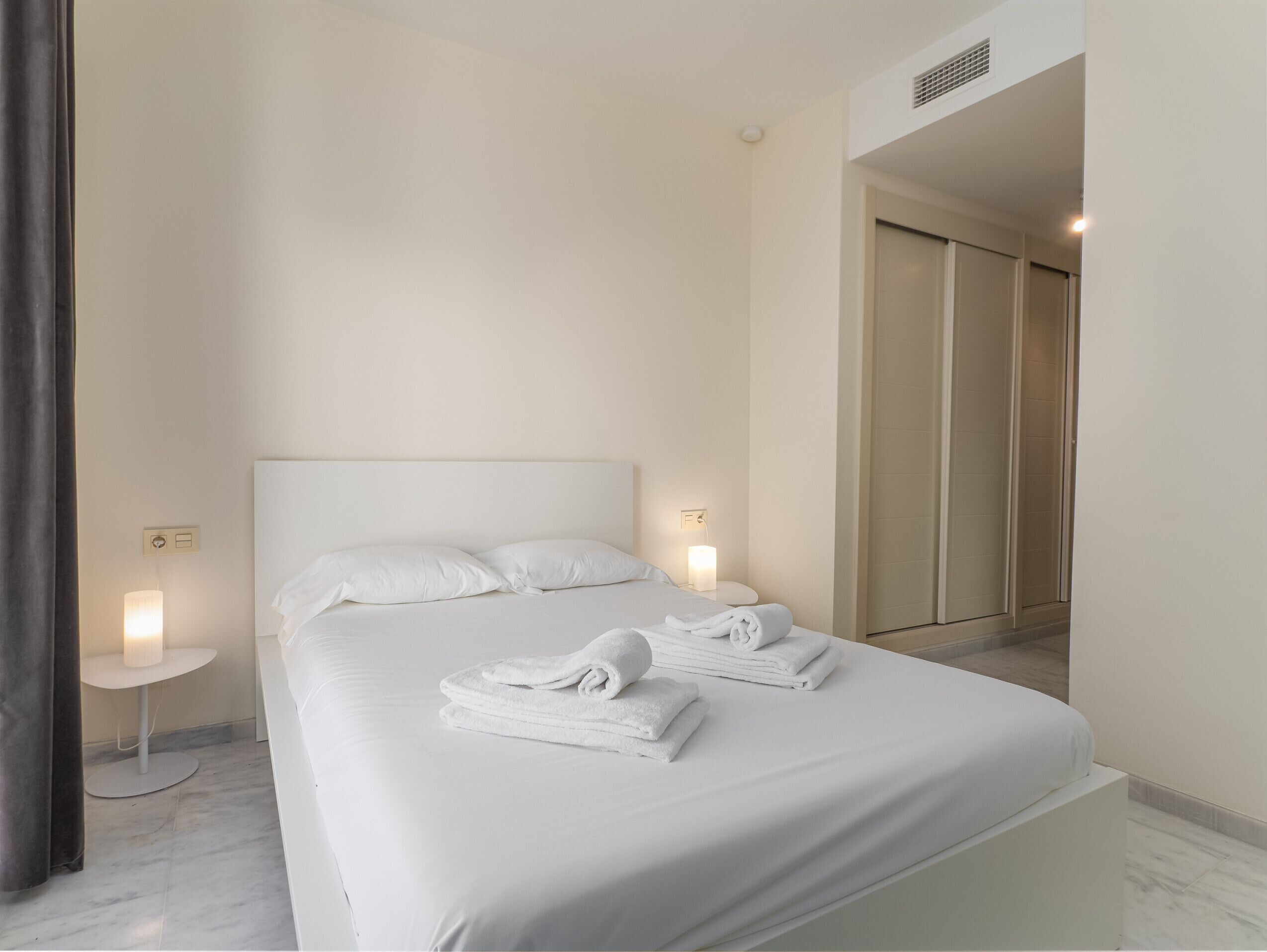 A modern hotel room with a large bed, two bedside tables, and a walk-in closet.