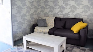 Een woonkamer met een donkere bank, een decoratieve plaid en een witte salontafel.