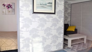Een kamer met een bed, een slaapbank, een klein tafeltje en een ingelijst kunstwerk aan de muur.