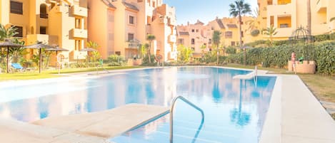 A swimming pool with a metal ladder, surrounded by palm trees and lounge chairs.