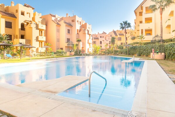 A swimming pool with a metal ladder, surrounded by palm trees and lounge chairs. - Duquesa Village 2114 Pool & Garden (Manilva)