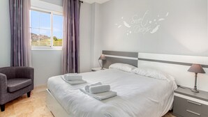 A hotel room with a bed, a chair, a nightstand, a lamp, and a wall with a decorative phrase. - Residencial Duquesa 2091 Manilva (Manilva)