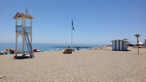 A beach with a lifeguard tower, a small blue and white building, and colorful umbrellas. - Residencial Duquesa 2091 Manilva (Manilva)