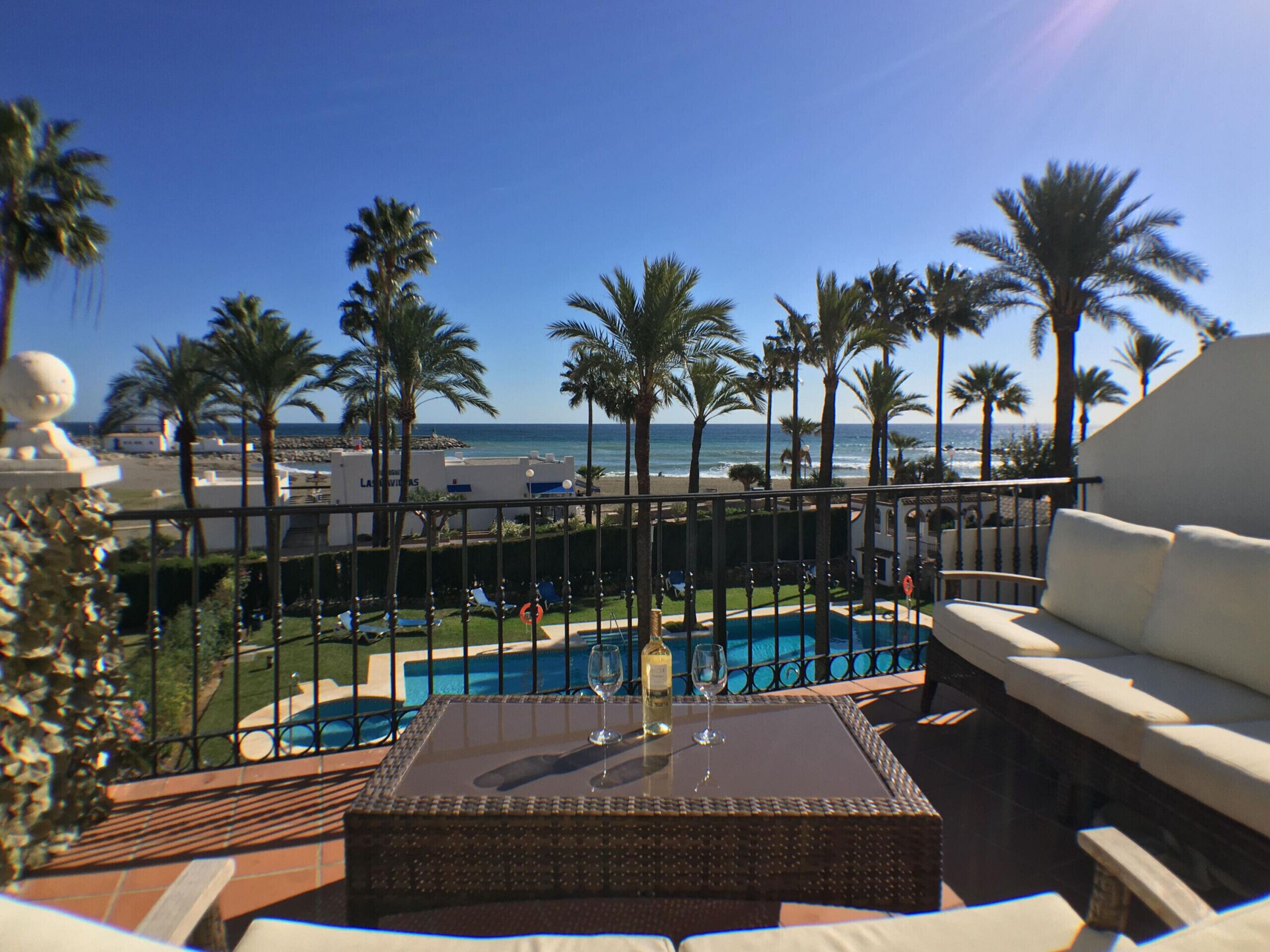 A poolside area with a view of the ocean, palm trees, and a fenced pool.