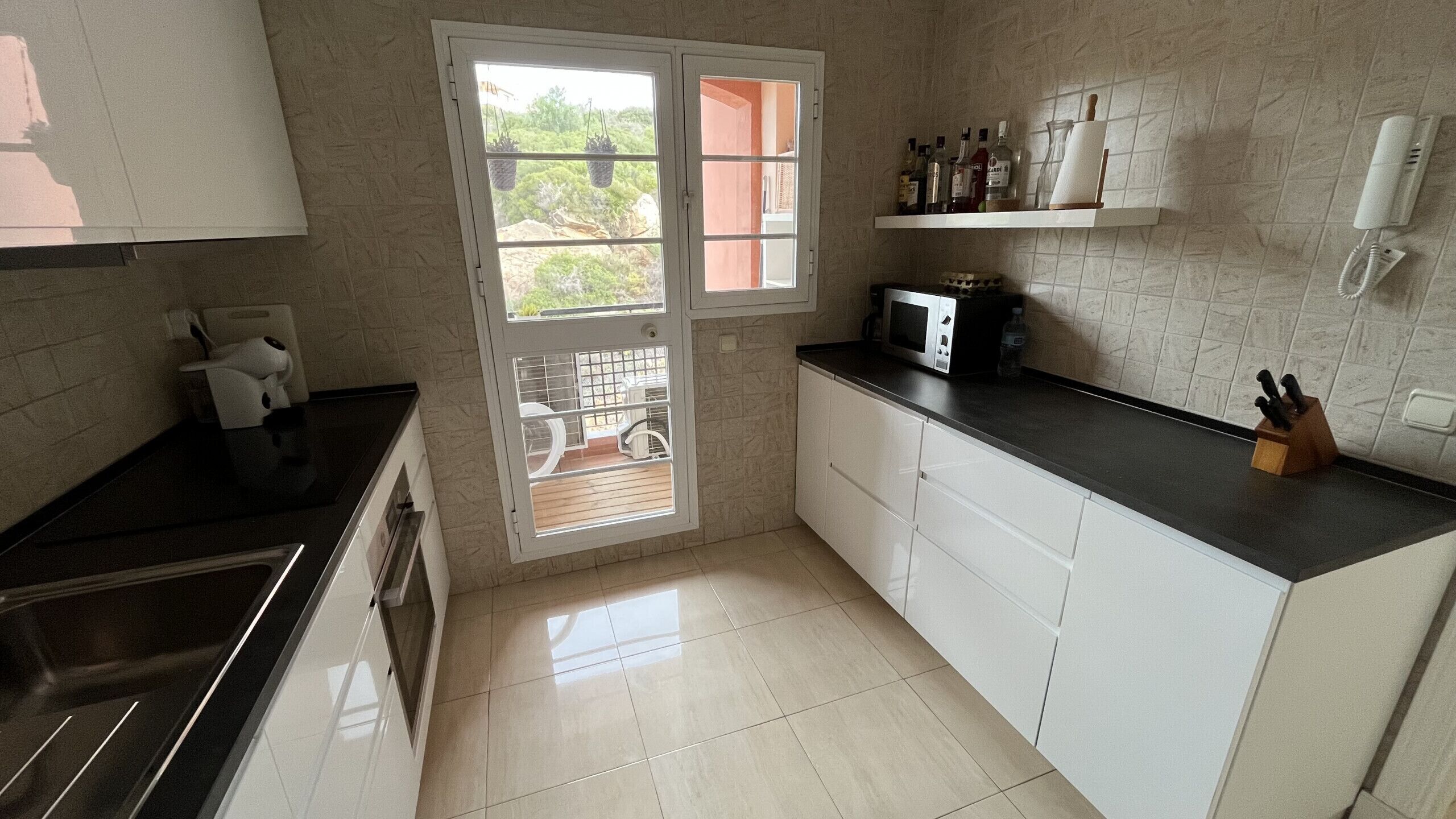A compact kitchen with white cabinets, a black countertop, a microwave, and a window with a view of greenery outside.