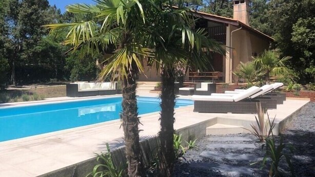 A pool area with lounge chairs, a palm tree, and a building with a chimney.