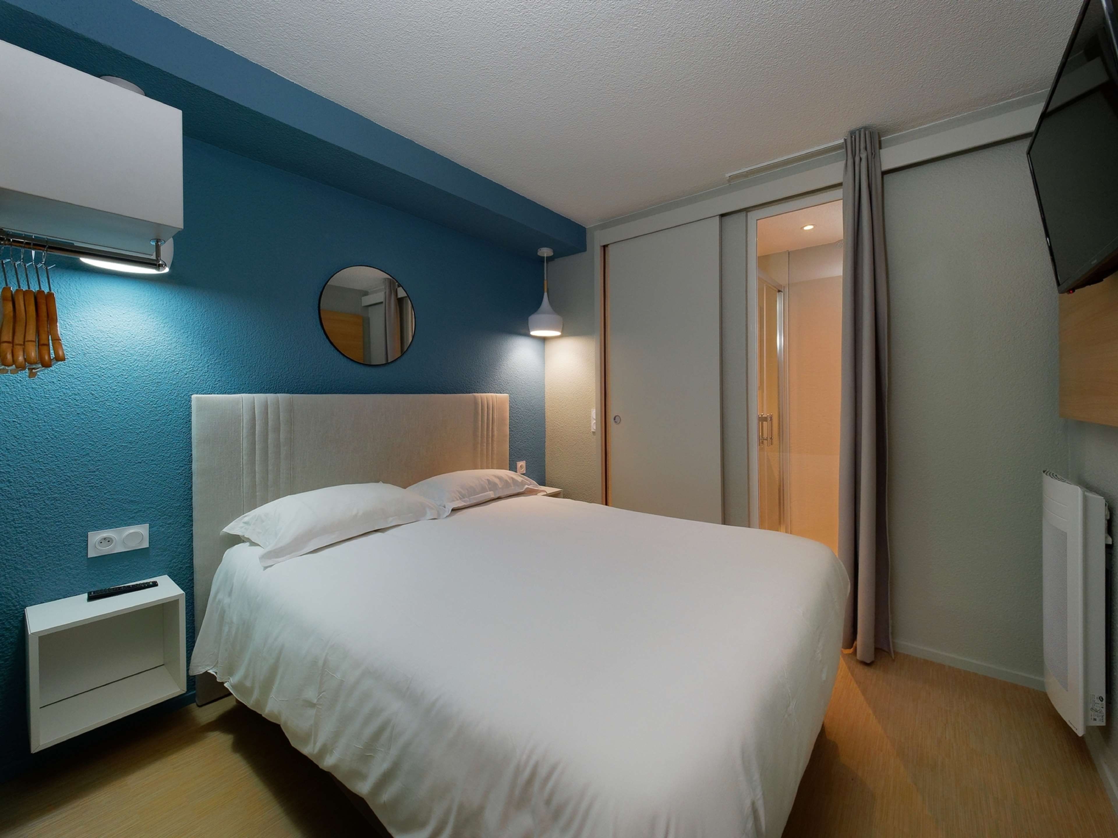 Une chambre d’hôtel avec un lit, un miroir rond, une table de chevet et une armoire.