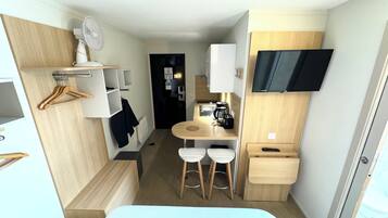 Habitació d'hotel senzilla amb llit, una cuineta petita, televisió i zona de seients amb tamborets.