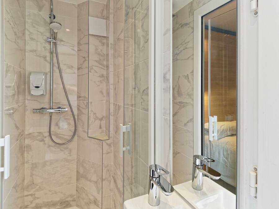 A modern bathroom with a glass-enclosed shower, a large mirror, and a white sink.