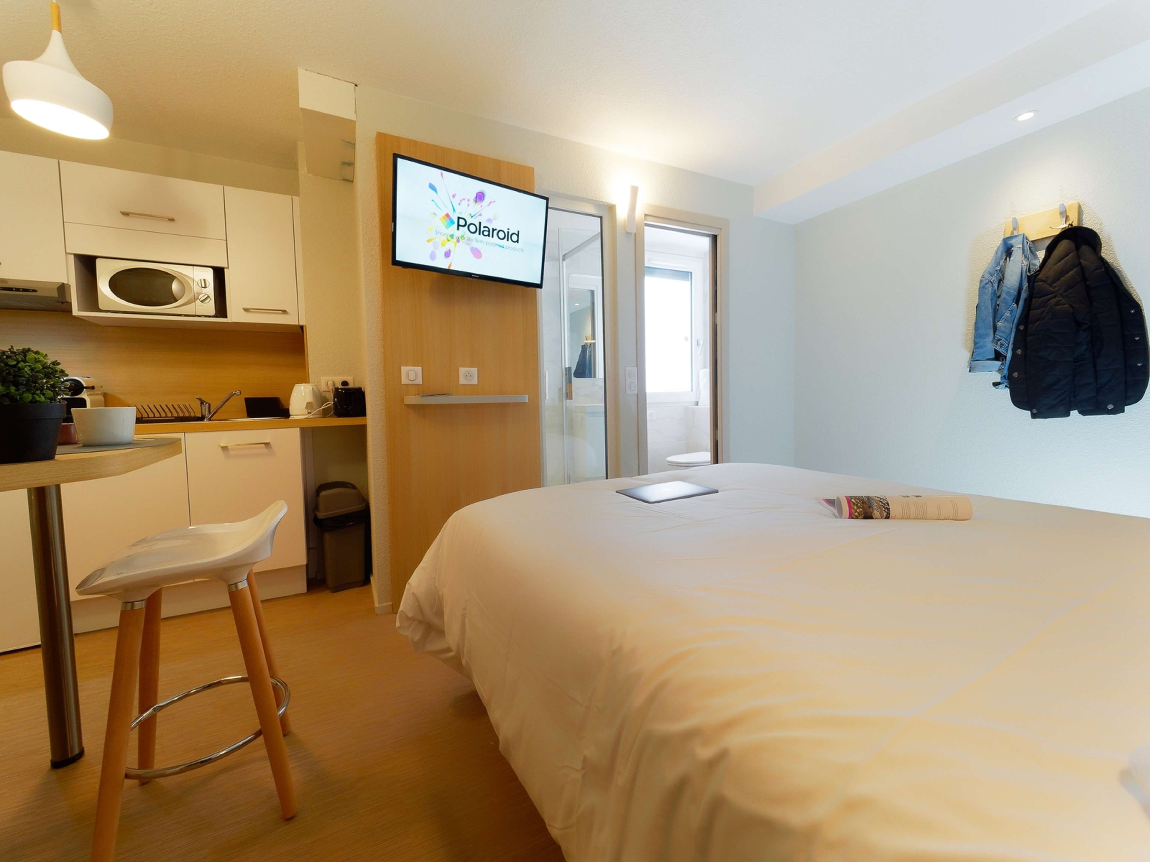 Una habitación de hotel moderna con una cama, un escritorio, una silla, un televisor y un perchero.