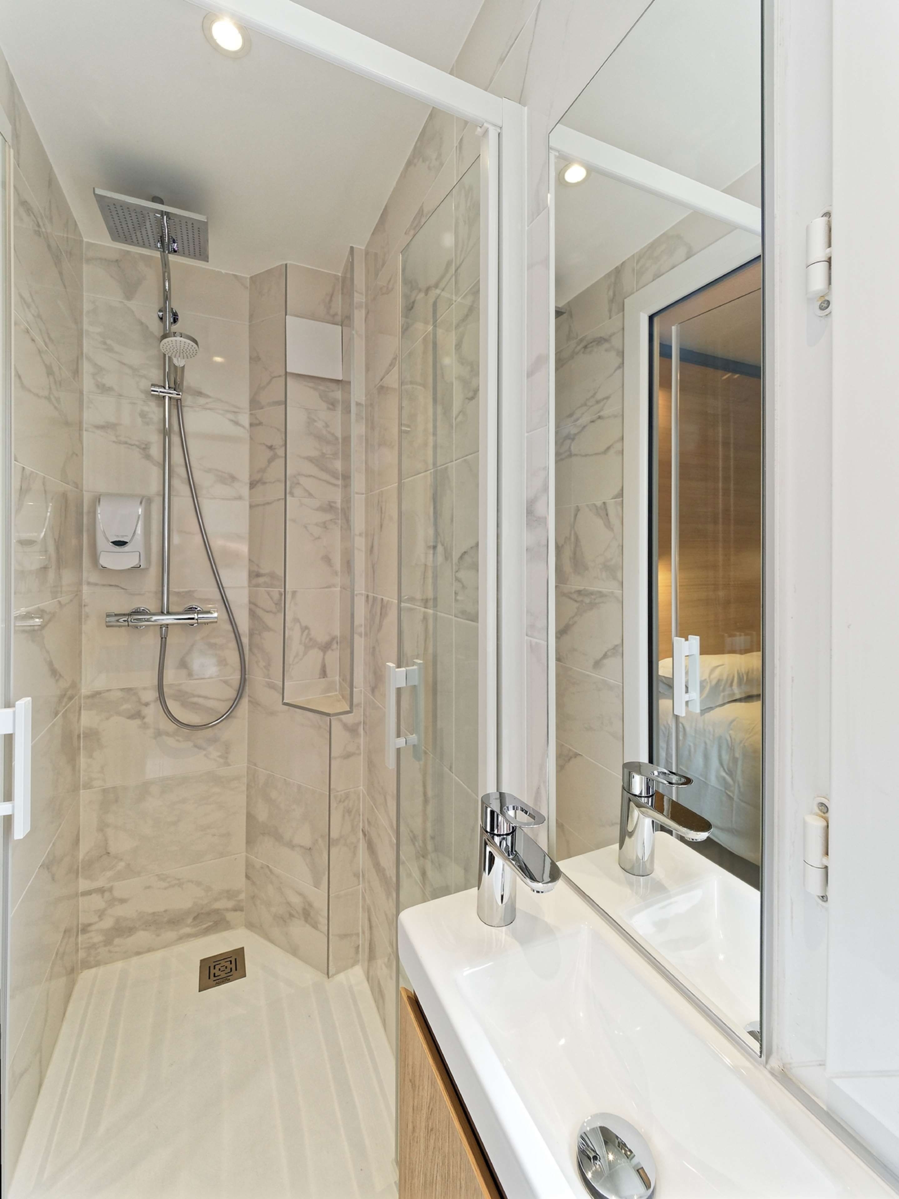 Une salle de bain moderne avec une douche à l’italienne, un grand miroir et un lavabo blanc.