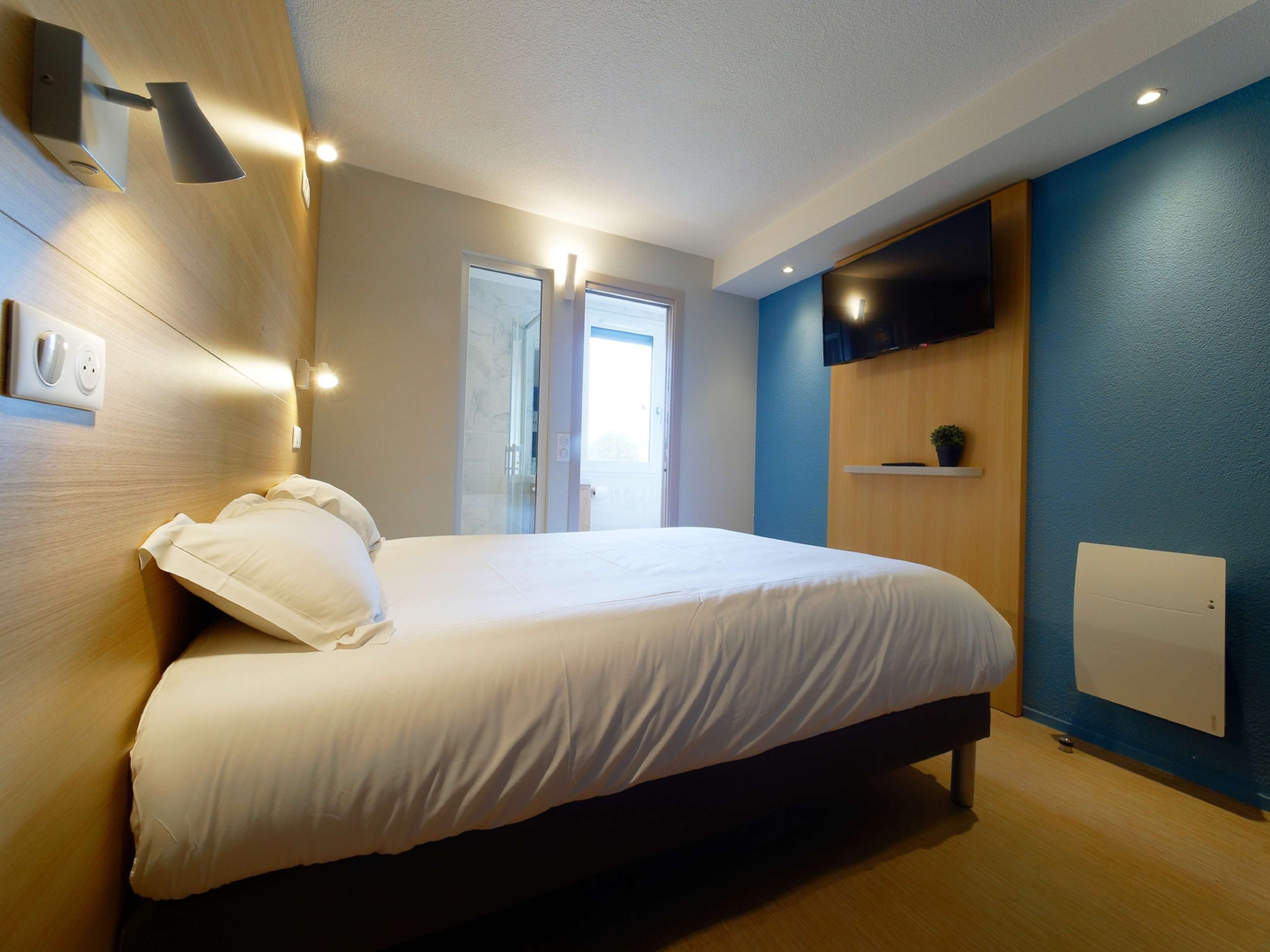 Ein modernes Schlafzimmer mit Bett, Nachttischlampen, einem Fernseher und einem Fenster.