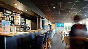 A modern bar area with a long counter, bar stools, and a television screen. - Kyriad Direct Saint Brieuc - Parc des Expositions (Tregueux)