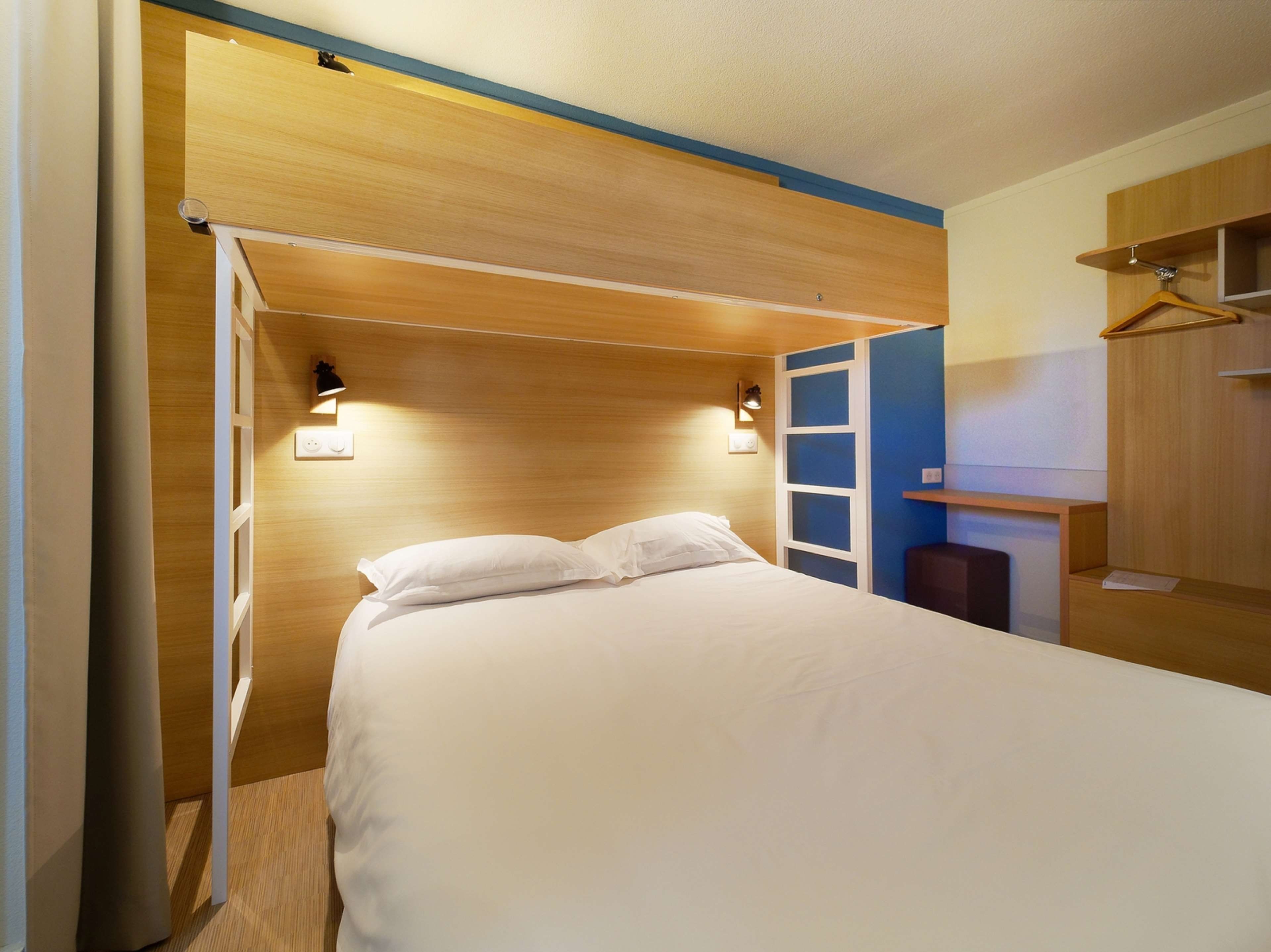 A bedroom with a bed, bedside lamps, a wardrobe, and a desk.