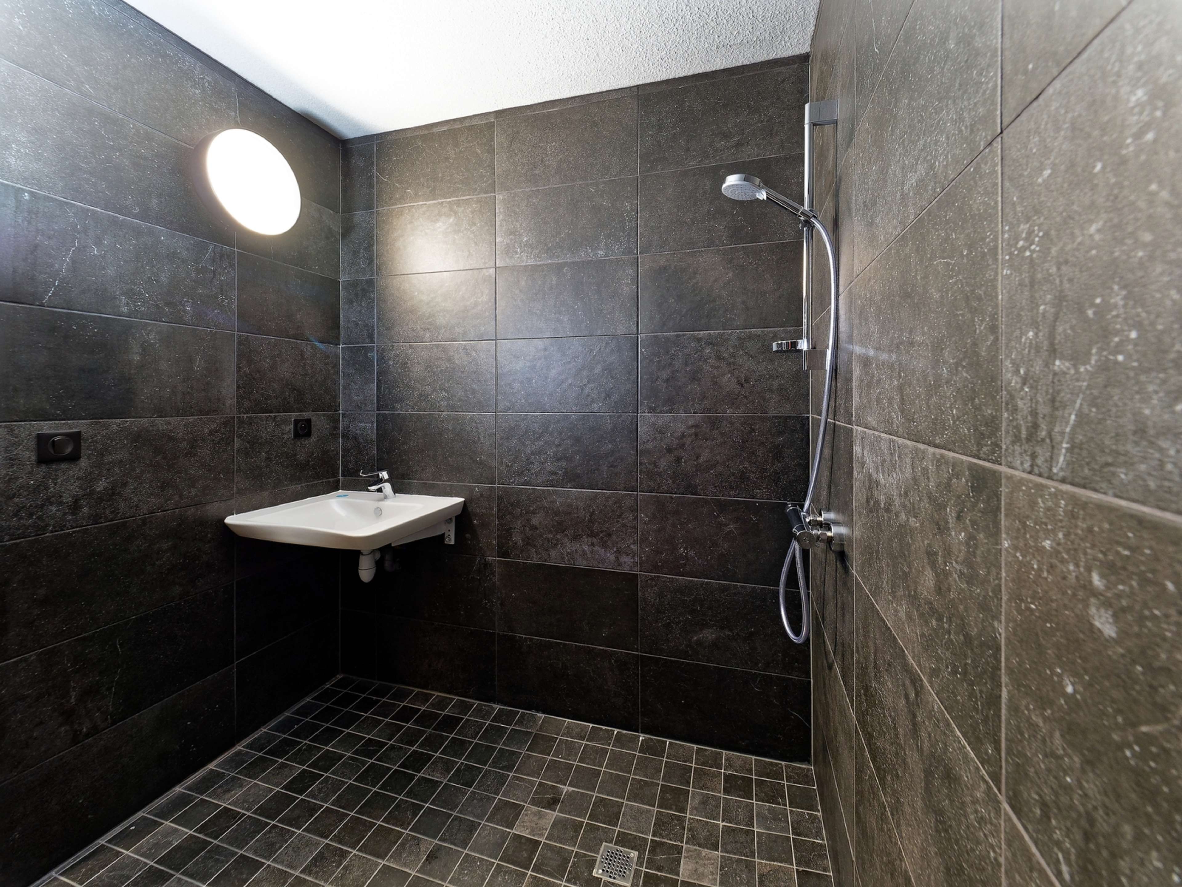 A bathroom with dark tiles, a white sink, and a shower.