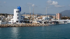 Un puerto deportivo con barcos, un faro y edificios de arquitectura mediterránea.