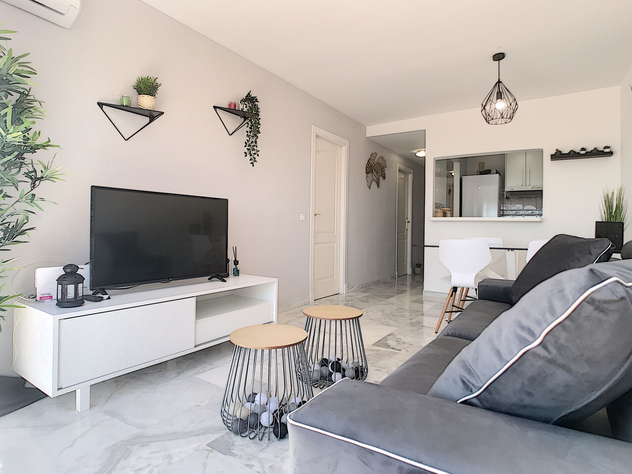 Uma sala de estar moderna com televisão de tela plana, um sofá, uma mesa de centro e um espaço de refeições com cozinha ao fundo.