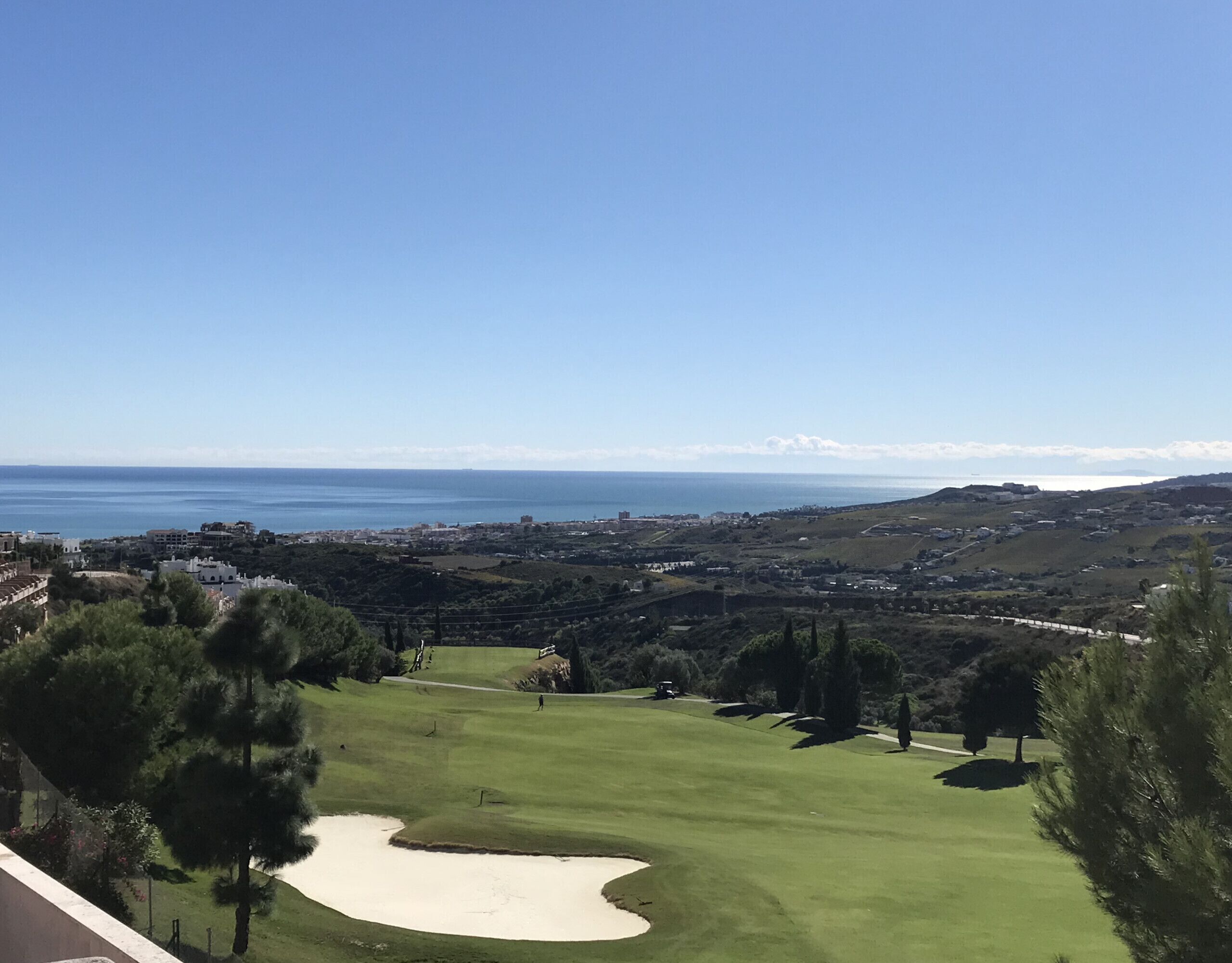A golf course with a view of the sea and distant buildings.