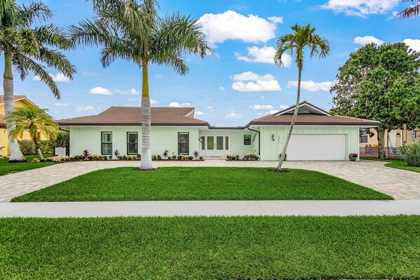 A two-story house with a front garage, a well-maintained lawn, and palm trees. - Fully Remodeled Single-Story Home w/Heated Pool and Boat Dock (Marco Island)