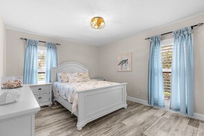 A bedroom with a bed, bedside tables, a nightstand, a window with curtains, a ceiling light fixture, and a wall-mounted artwork. - Fully Remodeled Single-Story Home w/Heated Pool and Boat Dock (Marco Island)