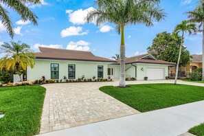 A residential house with a paved driveway, a well-maintained lawn, and palm trees. - Fully Remodeled Single-Story Home w/Heated Pool and Boat Dock (Marco Island)