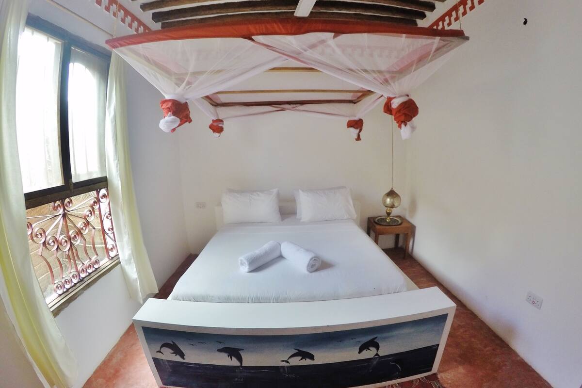 Un dormitorio con cama, mesita de noche, ventilador de techo y ventana con cortinas.