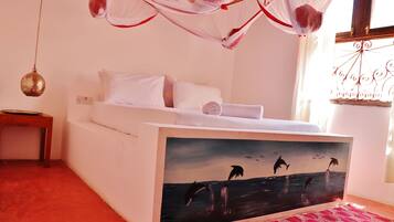 Un dormitorio con cama, una mesita de noche, una lámpara colgante y una ventana con cortinas.